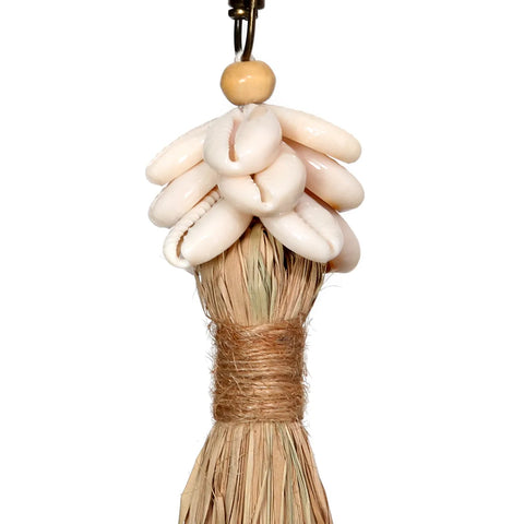 A decorative keychain exuding a bohemian atmosphere, featuring a cluster of white cowrie shells atop a bundle of dried grass, tastefully wrapped with twine. A small wooden bead and tassel complete this charming handmade piece.