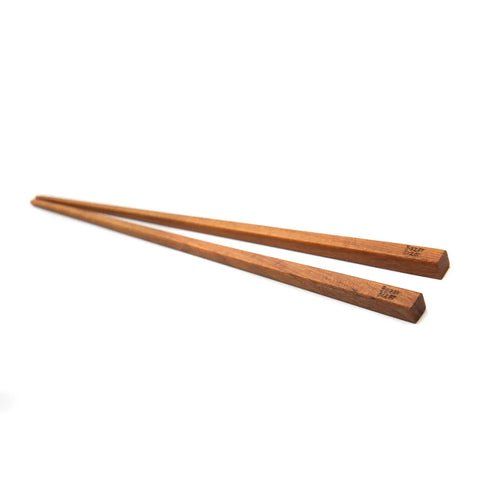 A pair of durable teak root chopsticks with a smooth finish and square shape, lying side by side on a white surface. The chopsticks have small black markings near the wider end, perfect for a classy table setting.