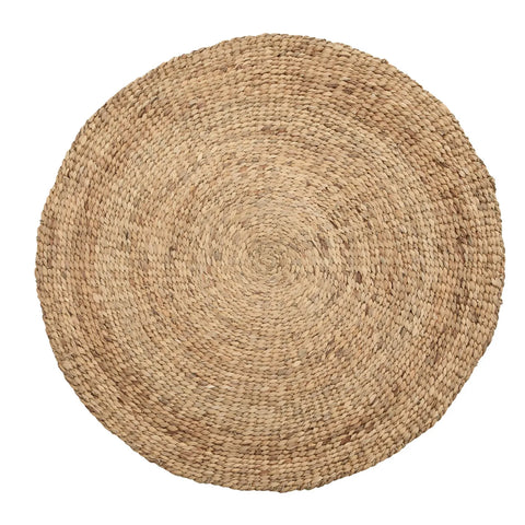 A round, woven jute rug with a natural, earthy texture and color, featuring a concentric circular pattern. The braided design evokes a boho aesthetic, perfect for enhancing home decor with a rustic touch.