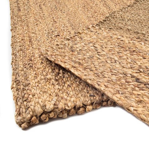 Close-up of a woven jute rug, radiating a natural vibe with its earthy texture. The pattern of tightly braided fibers offers a handmade appeal, creating a rustic and organic appearance. This layered design showcases the rug's thickness and durability.