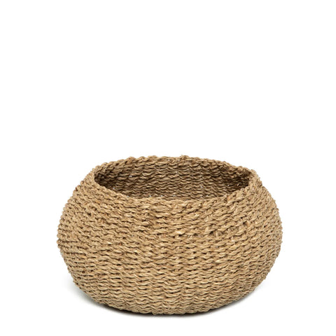 A round, woven seagrass basket made from natural fibers sits against a plain white background. The basket features a wide opening and a textured surface, showcasing its handmade appearance as an ideal storage container.