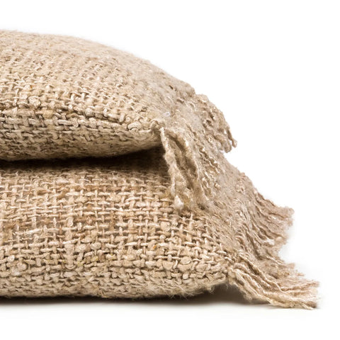 Two stacked burlap sacks, reminiscent of handmade textiles, with frayed edges against a plain white background. The texture of the coarse woven fabric is clearly visible, highlighting the rustic appearance of the material.