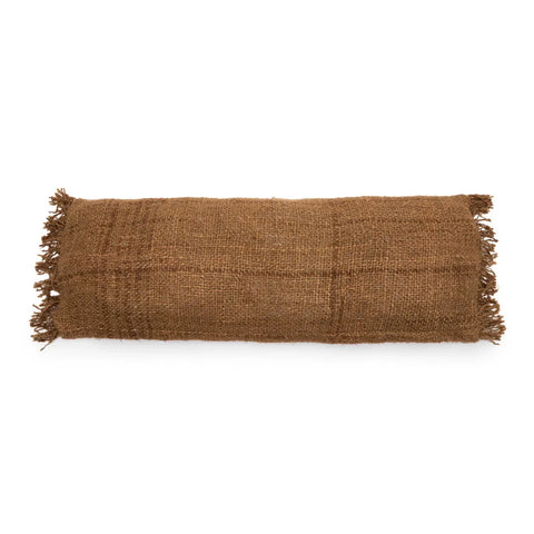 A rectangular brown burlap pillow with a textured surface and frayed edges on the shorter sides exudes a boho vibe, resting against a white background.