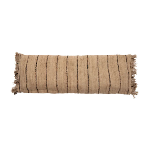 A rectangular beige pillow with black vertical stripes and fringe details on the sides, this unique textile product exudes a boho vibe. The texture appears woven, giving it a rustic look.