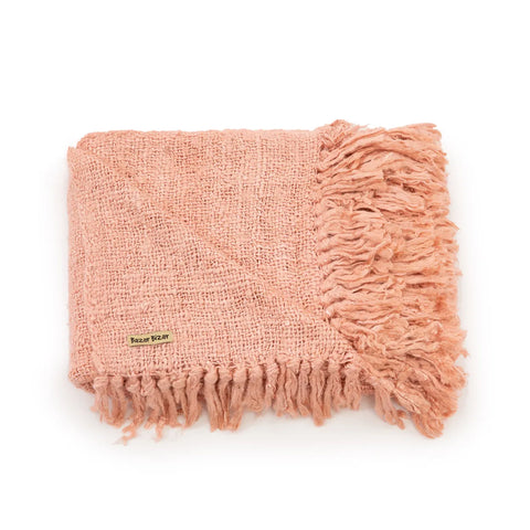 A folded pink textured blanket with fringed edges adds a touch of elegance to your home interior. The blanket's label is visible, displaying Better Living branding, and its luxury hand-woven cotton finish offers a cozy and sophisticated vibe.