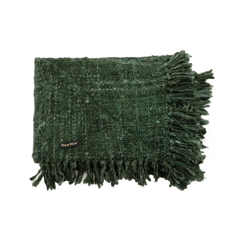 A textured green throw blanket made from luxury hand-woven cotton, with fringe details along the edges, folded neatly. Its small tag reads Pixxy Wuzzy.