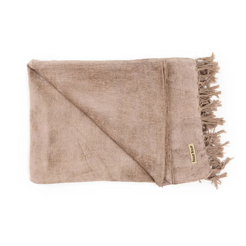 A folded, light brown woven throw blanket graces your home with its fringed edges and a small tag on one side. This luxury hand-woven textile product boasts a soft, textured fabric with a silk look, adding an elegant touch to any space.