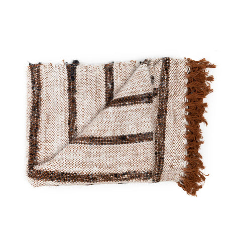 A folded woven blanket with a textured, speckled pattern in white, brown, and black combines a luxury hand woven cotton plaid feel. The Bohemian White blanket features a striped design with brown fringe on one edge.