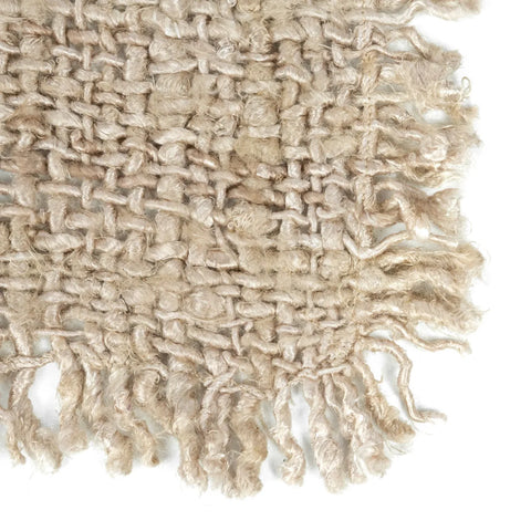 Close-up of a woven cotton placemat with a luxurious texture and textured appearance. The edges are uneven and frayed, giving it an organic, rustic look. The fibers vary in thickness, creating a tightly knit pattern. The color is a soft, natural beige.