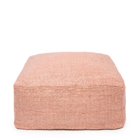 A square, soft pink pouf made of textured, hand-dyed fabric is shown against a white background. This charming cotton pouffe serves as a delightful home accessory, adding an elegant touch to any space.