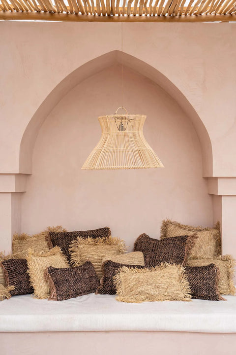 Cozy seating nook with a soft, hand-dyed cotton cushion and numerous textured cushions in shades of brown and beige. An arched wall forms the background with a wicker lamp hanging above, while the slatted wooden ceiling enhances the relaxed, boho vibe ambiance.