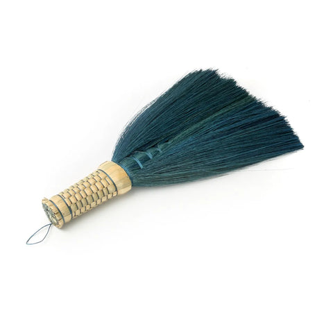 A Boho-inspired handheld broom with a woven bamboo handle and dark green bristles showcases the beauty of Indonesian hand sweepers against a plain white background.