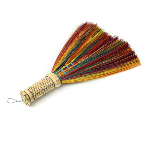 A Boho hand broom with a woven wooden handle and colorful bristles, including shades of red, yellow, green, and blue. The sweeping brushes fan out for a vibrant, decorative effect. Inspired by Indonesian hand sweepers, it includes a loop for hanging.