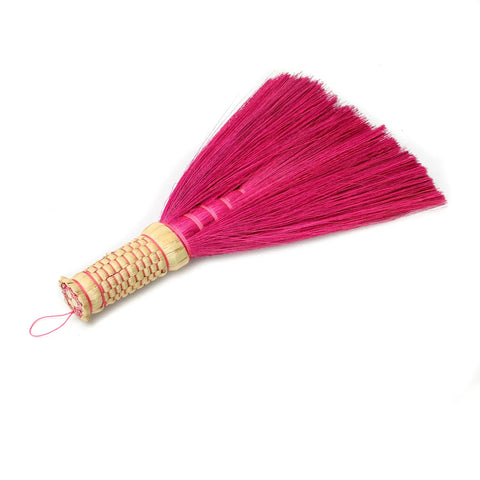 A handmade boho must-have broom with vibrant pink bristles and a woven bamboo handle, isolated on a white background.