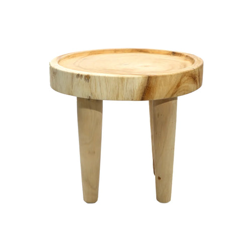 A small, round wooden stool crafted from suar wood with three tapered legs. The natural wood finish showcases a light tone and visible grain patterns, embodying a natural style.