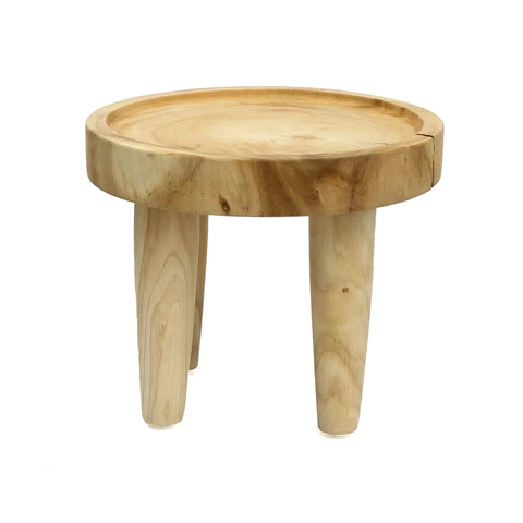 A small wooden stool crafted from suar wood with a round top and three legs, showcasing a natural wood grain finish. The stool has a simple, rustic design perfect for boho spaces, suitable as a side table or seating.