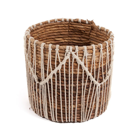 The Macra-Mazing Basket is a round woven piece crafted from natural brown fibers, showcasing an intricate geometric pattern with white rope. Its subtle macramé design adds a delicate touch to the exterior, making it a stunning and functional work of art.