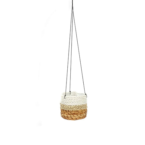 A small, round hanging basket woven from banana leaf with natural tones of white and beige is suspended by two thin black cords against a plain white background. Perfect for displaying indoor plants, it adds a touch of nature to any room.