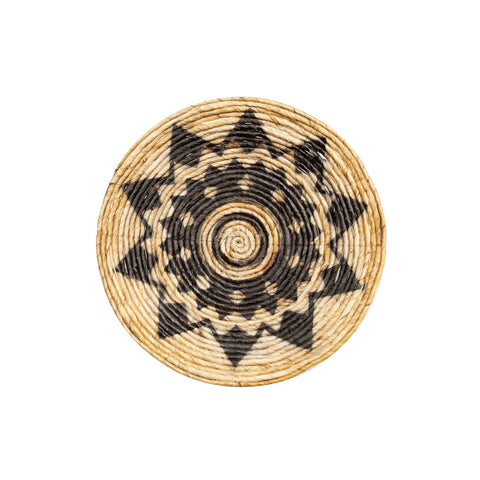 A round woven basket with a geometric sunburst pattern, this handwoven plate exudes a natural vibe. The alternating black and natural colors create a bold design, featuring a central spiral and radiating triangle shapes, making it ideal for an ethnic wall display.