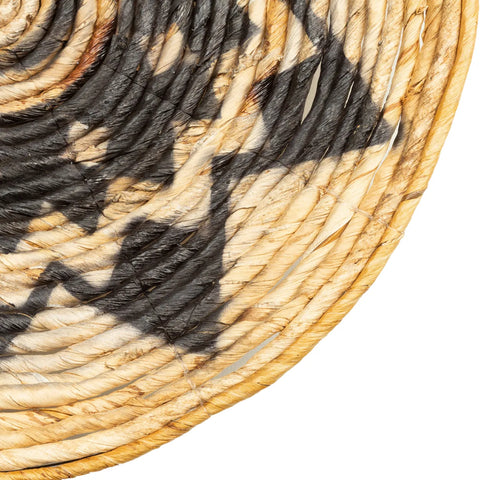 Close-up of a handwoven basket with a spiral pattern, perfect for an ethnic wall display. The basket features natural beige tones with darker brown and black geometric designs. The texture of the woven material is visible, exuding a natural vibe and showcasing intricate craftsmanship.