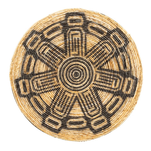 A round, woven basket lid with an intricate star-like pattern in black and natural straw colors exudes a natural vibe. The design, ideal for an ethnic wall display, features repeated geometric shapes radiating from the center.