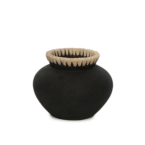 A black, round terracotta vase with a wide body and narrow opening, featuring a textured surface and coastal vibes accentuated by a detailed, woven beige raffia rim.