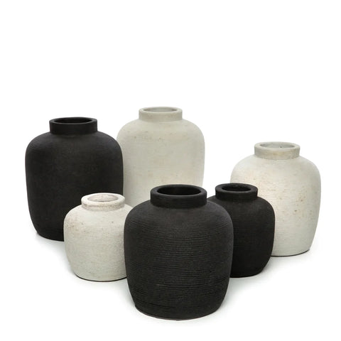 A group of six textured ceramic vases in black and white hues are arranged together, their ribbed textures adding depth. The vases, perfect for displaying dried flowers, vary in size and shape with rounded bodies and narrow openings, set against a plain white background.