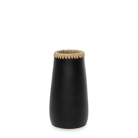 A tall, black terracotta vase with a smooth surface and a jagged, beige rim is beautifully complemented by dried flowers, all set against a plain white background.