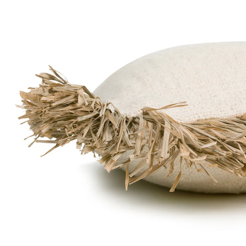 This Raffia fringed cushion is a close-up of a round, beige pillow with textured, woven fabric. The soft furnishings feature straw-like fibers along the edge, offering a natural and rustic appearance with a boho touch. The background is plain white.