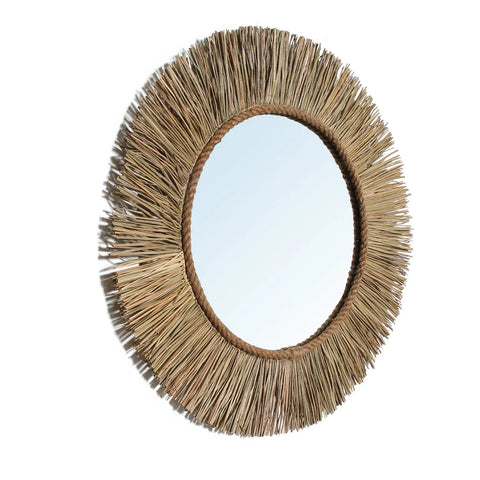 A natural mirror featuring a decorative frame crafted from straw-like materials, arranged in a sunburst pattern, exudes an earthy boho vibe against a crisp white background.