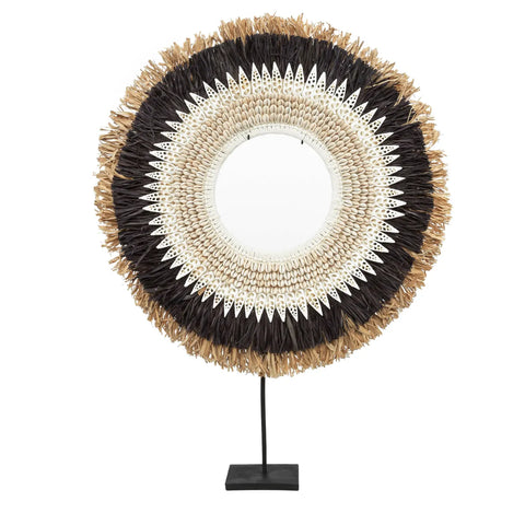 A decorative item, this circular piece features layers of textured feathers and hand-placed shells in black, white, and brown. It is elegantly mounted on a black stand.