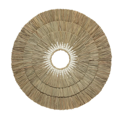 A flat, round wall decoration made of natural tan reeds or straw arranged in concentric layers, forming a coastal, bohemian design with a small central opening.