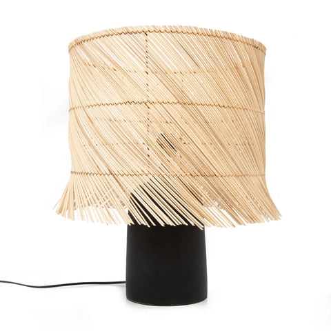 This table lamp boasts a black cylindrical base and a large, woven bamboo-style shade that exudes a boho look. The diagonal strands form an open, airy design for cozy light. A visible cord extends elegantly from the base, complementing its artistic aesthetic.