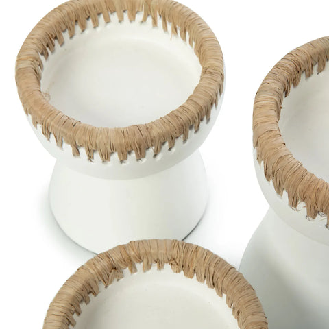 Close-up of three white ceramic stools with beige woven raffia accents around the edges. They have a slightly concave top and flared bases, creating a modern and rustic look.