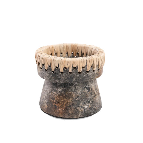 A rustic, round stone container with a flared base and a woven fiber rim sits against a white background. Resembling an antique grey candle holder, it has a textured surface with shades of gray and brown, enhancing its earthy terracotta appearance.