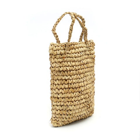 A woven straw tote bag with two short handles exudes a boho vibe, featuring a natural, textured appearance. Perfectly paired with your summer table setting, it is shown against a plain white background.