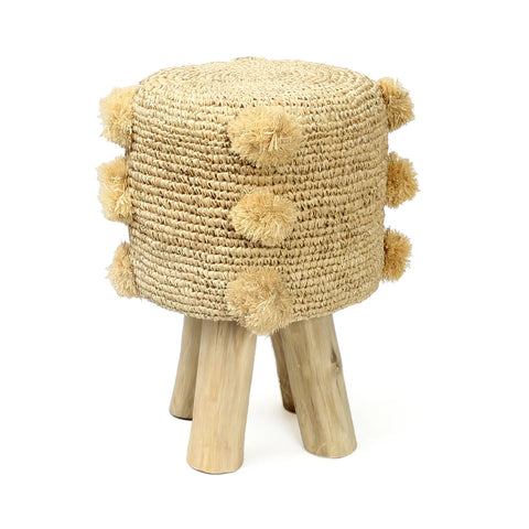 A round raffia stool with tassel decorations on the sides features four teak wood legs, exuding a summer vibe.