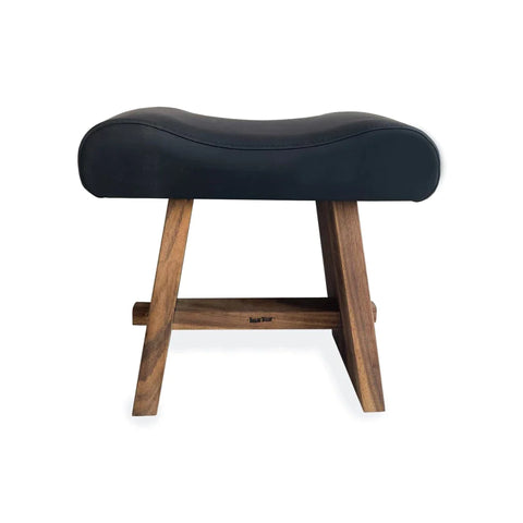 A modern stool with a sleek, matte leather cushioned seat and wooden legs in a natural finish, featuring a minimalistic, contemporary design. The Suar wood legs are crossed with horizontal support.