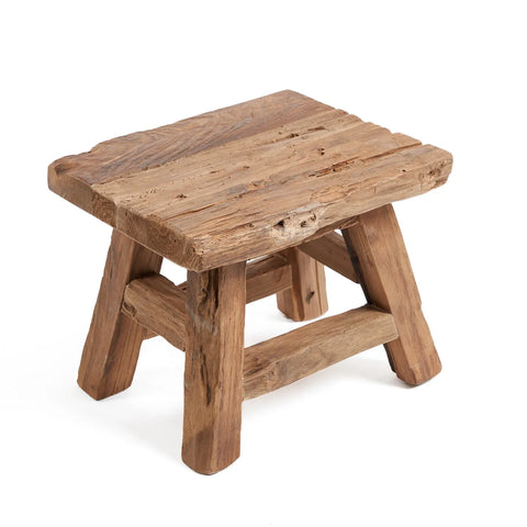 A small, rustic wooden stool crafted from reclaimed teak wood features a square seat and sturdy, angled legs. The weathered wood offers a vintage look, emphasizing its sustainable design.