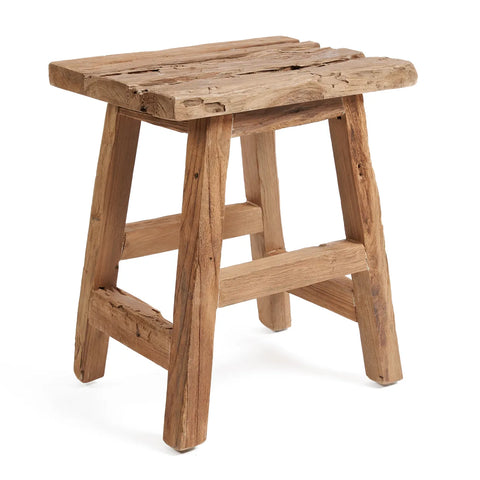 A rustic wooden stool with a simple, sturdy design crafted from reclaimed teak wood. The seat and legs boast a natural, unfinished look that highlights the rough, textured wood. Its construction is basic yet thoughtful, incorporating two crossbars for support in this sustainable design.