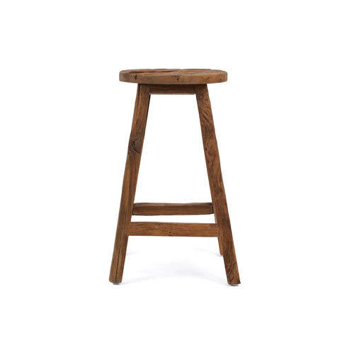 A rustic bar stool crafted from reclaimed teak wood features three legs and a round seat, all showcasing the natural, unpolished finish. The design is simple yet timeless, with a supporting crossbar between the legs. The image sits against a white background.