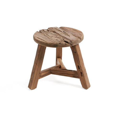 A rustic wooden stool with a round, weathered seat and three sturdy legs connected by a triangular support, crafted from reclaimed teak wood. The natural wood grain and texture enhance its aged, handmade appearance, adding character to any space.