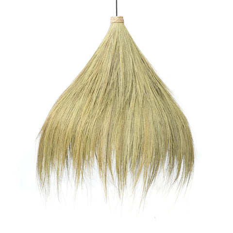 A broom with long, yellowish bristles forms a fan-like shape against a plain white background, evoking a boho vibe. The handle is partially visible at the top, accentuating its natural grass-inspired charm.