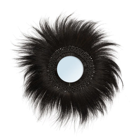 A round wall mirror with a decorative black feathery frame, resembling sun rays, exudes boho charm on a crisp white background.