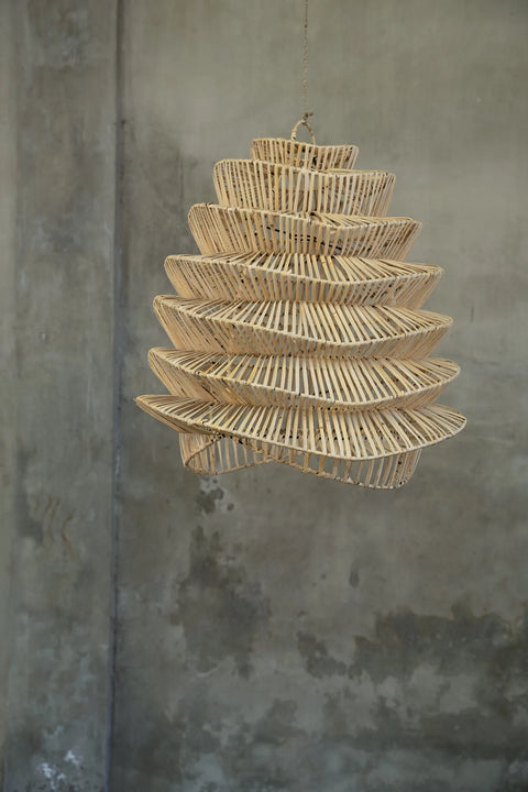 A handcrafted, spiral-shaped bamboo pendant light hangs against a textured, gray wall, showcasing an intricate design that creates a modern and artistic look in the space.