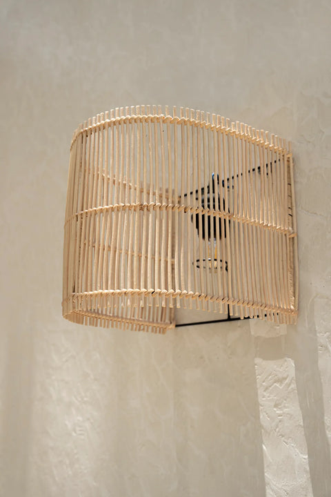 A wall-mounted lamp with a curved, rattan woven bamboo shade casts soft shadows on a textured white wall.