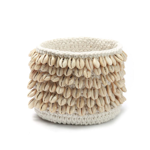 A decorative round basket adorned with rows of small, pale cowrie shells makes a stunning piece of home decor. Woven from natural fiber, it provides a textured contrast to the shiny, smooth shells. Perfect as a unique gift, it rests elegantly against a plain white background.