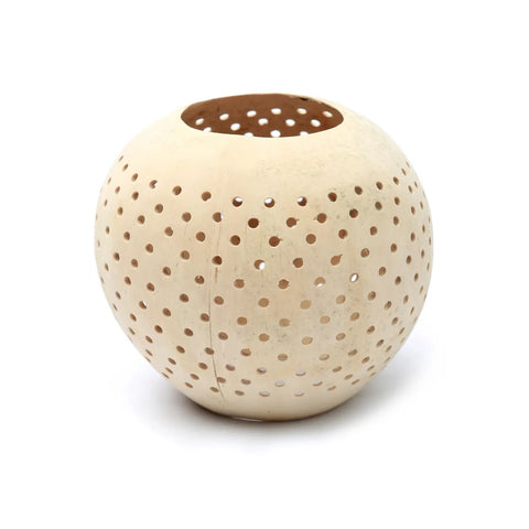 A handcrafted, round beige ceramic orb with evenly spaced small holes forms a perforated design. The top is open, revealing a hollow interior ideal as an eco-friendly coconut candle holder.