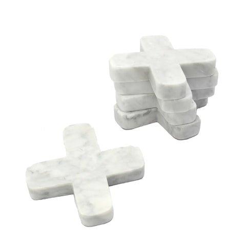 A stack of white, cross-shaped marble coasters elegantly complements any table setting, with one coaster lying flat beside the stack on a plain background.