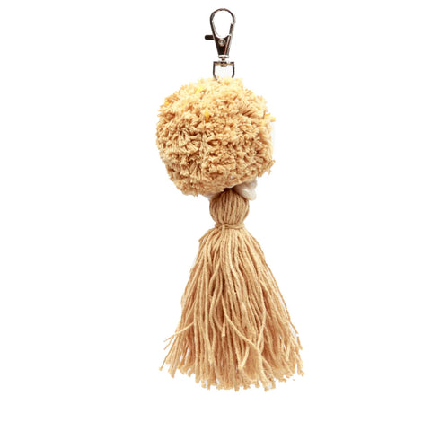 A pompom keychain adorned with a fluffy, round beige pom-pom at the top and long cotton tassels hanging below. It features a metal clasp for easy attachment.